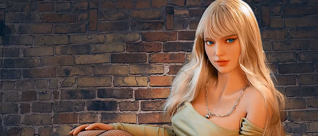 Blonde Sexpuppe mit realistischen Formen, sitzend vor einer Ziegelwand. Klicken Sie, um alle Sexpuppen anzusehen.